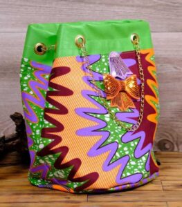 ankara sequin bucket bag in multicolor Ankara wax fabric with zigzag print, green faux leather trim, gold chain strap, and sequin bow embellishment.