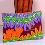 Ankara tropical blaze clutch in green, purple, and burgundy Ankara wax fabric with orange embroidered appliqués, sleek silhouette, and gold boutique logo.