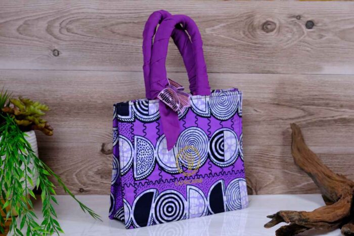 ankara violet spiral handbag in vivid violet Ankara wax fabric with black, white, and lilac spiral motifs, padded handles, and sequined butterfly accent.