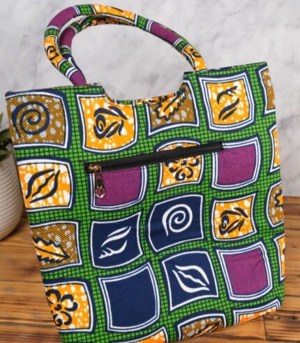 ankara geo motif tote in green, navy, mustard, and purple Ankara wax fabric with geometric patchwork, padded handles, and front zipper pocket.